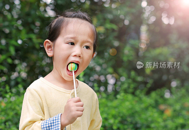 小女孩喜欢在公园里吃棒棒糖。