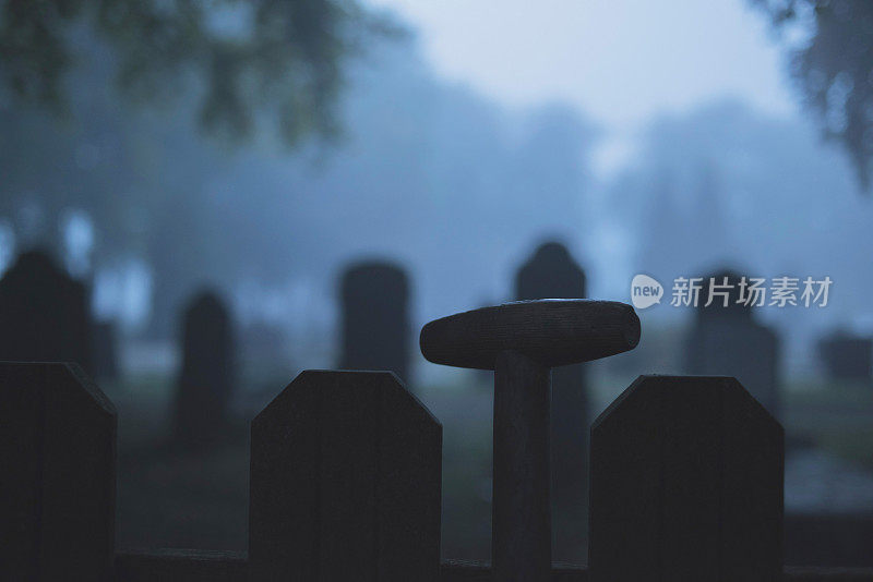 薄雾中，铁锹柄对着墓地的栅栏。