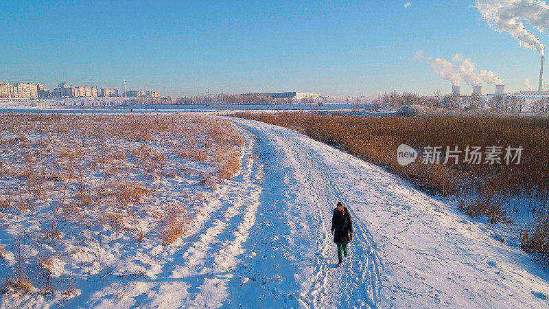 那个年轻的女人在白雪覆盖的乡村道路上奔跑和行走。低空无人机照片。