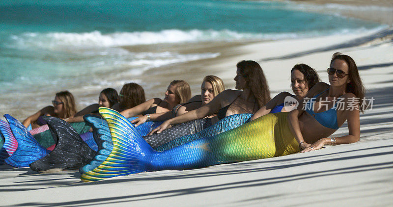 一群长着美人鱼尾巴的女人在热带海滩上摆姿势