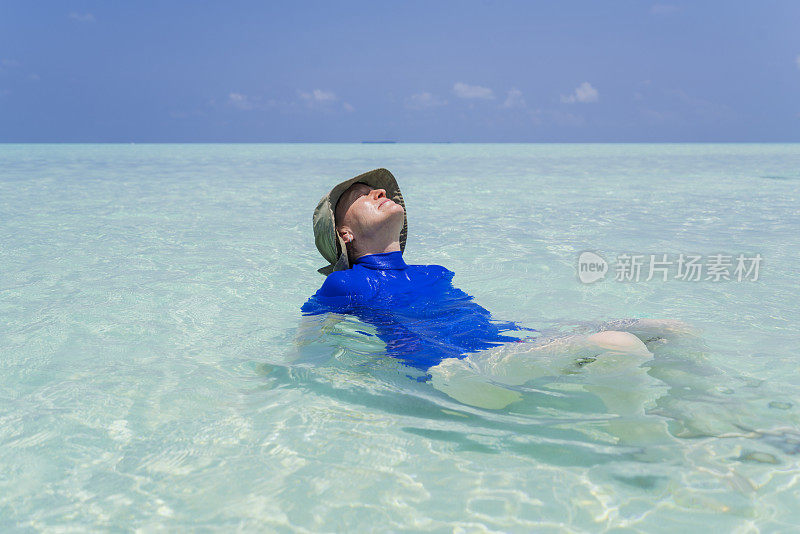 老年妇女享受躺在浅水和看太阳在小岛屿海滩在四月，马尔代夫