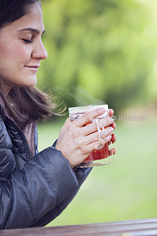 美丽的女人感到寒冷，喝草药茶在户外。