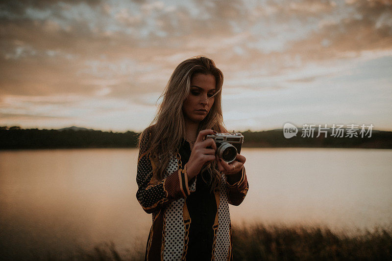 年轻女子在湖边用老式相机拍照