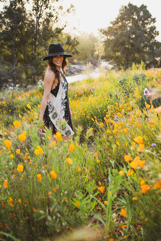 美丽的年轻西班牙女子戴着帽子微笑着站在罂粟花丛中