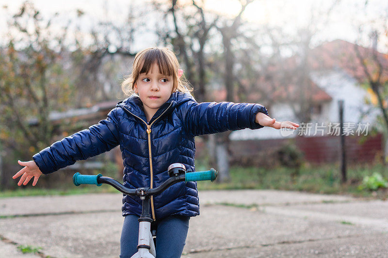 一个伸出双臂的小女孩坐在户外的自行车上。