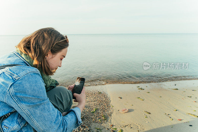 年轻的独自旅行者在海滩上用智能手机拍水母