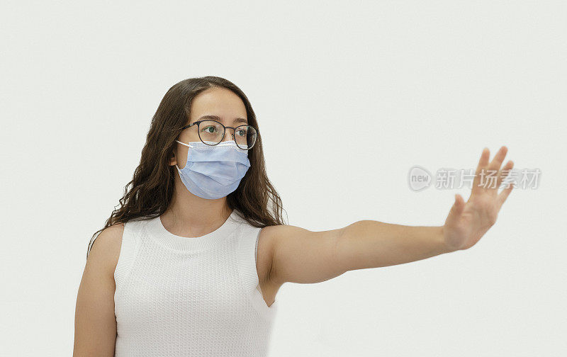 十多岁的女孩在病毒流行期间戴着防护口罩，用手势示意停止。