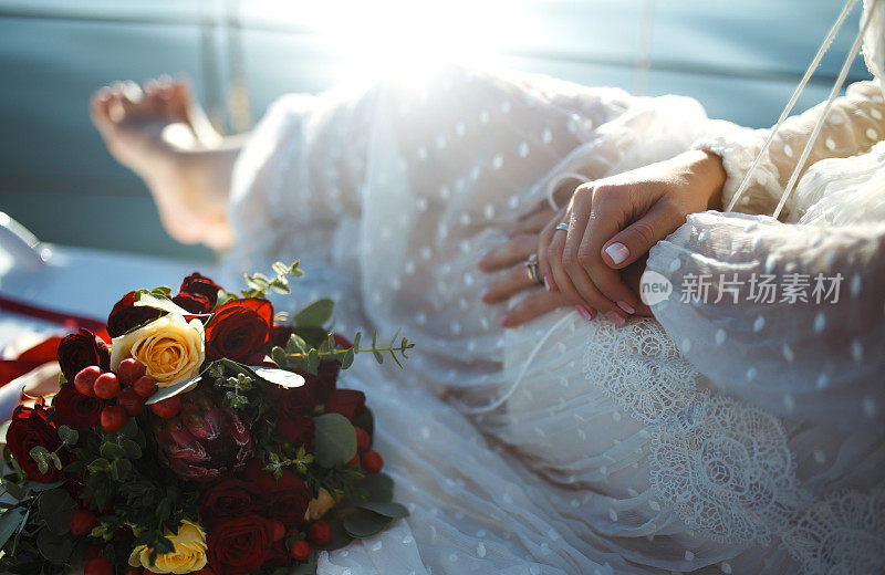 美丽时尚的新娘与婚礼花束在豪华的蕾丝白色礼服在游艇板在海上。