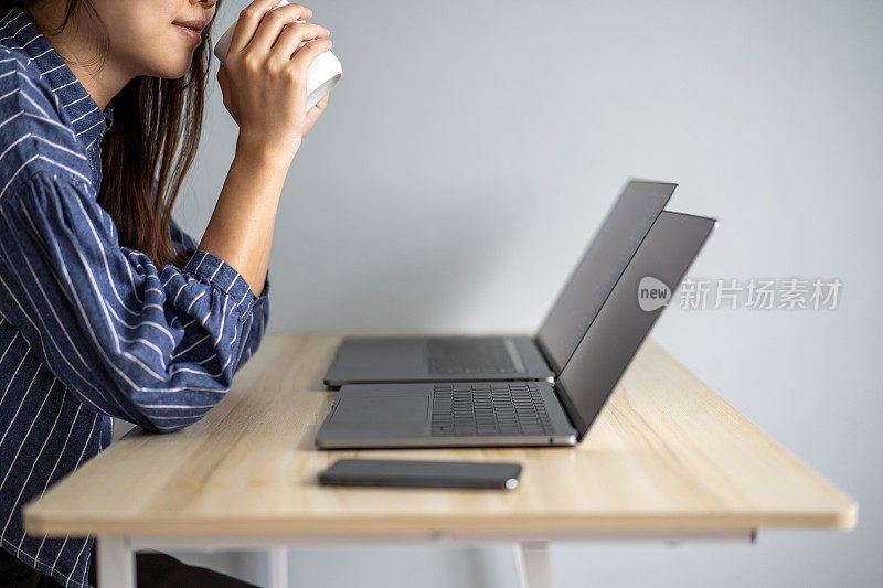 年轻女子在家里用两台笔记本电脑多任务工作
