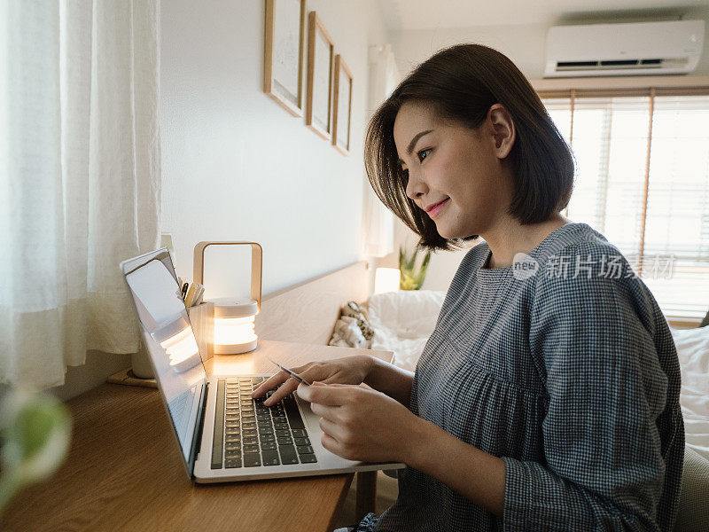 年轻女子在家里放松的时候使用笔记本电脑和信用卡