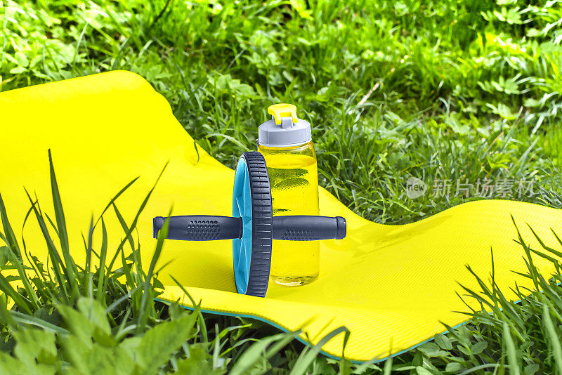 一个体操车轮的新闻界和一个运动瓶装水在瑜伽垫上在自然的背景。
