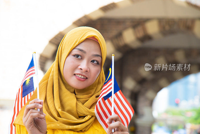 年轻的马来西亚妇女挥舞着马来西亚国旗，带着高昂的爱国主义精神庆祝独立日