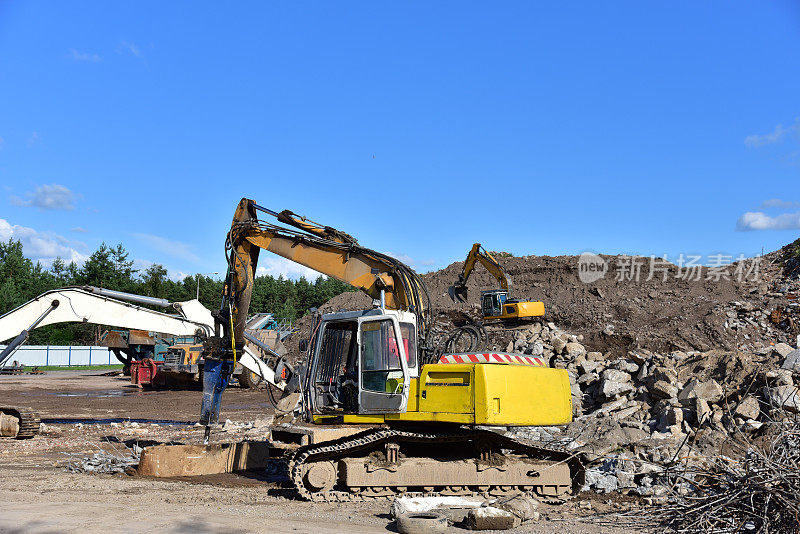挖掘机与液压破碎机锤破坏混凝土和硬岩石在垃圾填埋场。建筑废物的处置。从拆除中回收混凝土和沥青的手提钻
