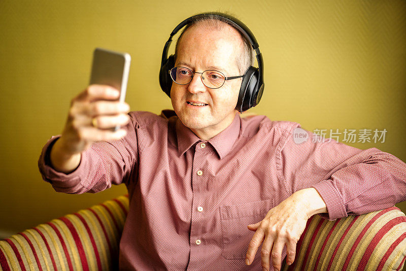 一个中年男子拿着手机坐在沙发上，戴着耳机和同事们进行视频会议