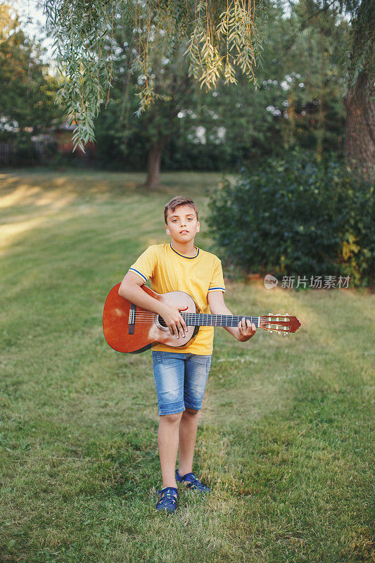 听力不佳的少年在户外弹吉他。带着助听器的孩子在公园里演奏音乐和唱歌。儿童爱好艺术活动。真实的童年的时刻。