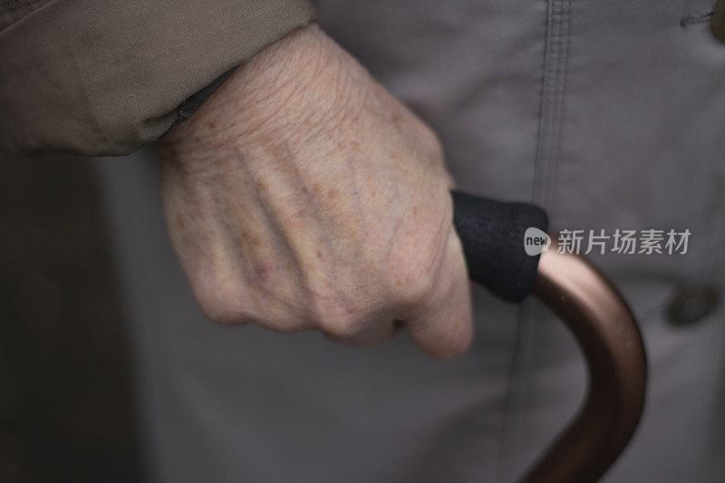 一位老妇人的手拄着拐杖。