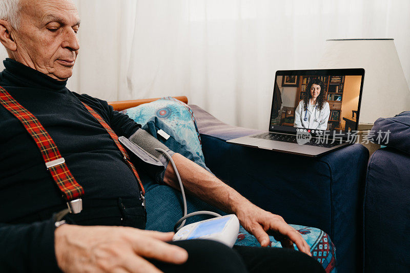 在和女医生视频通话期间，一位年长的男子在家里的沙发上检查自己的血压