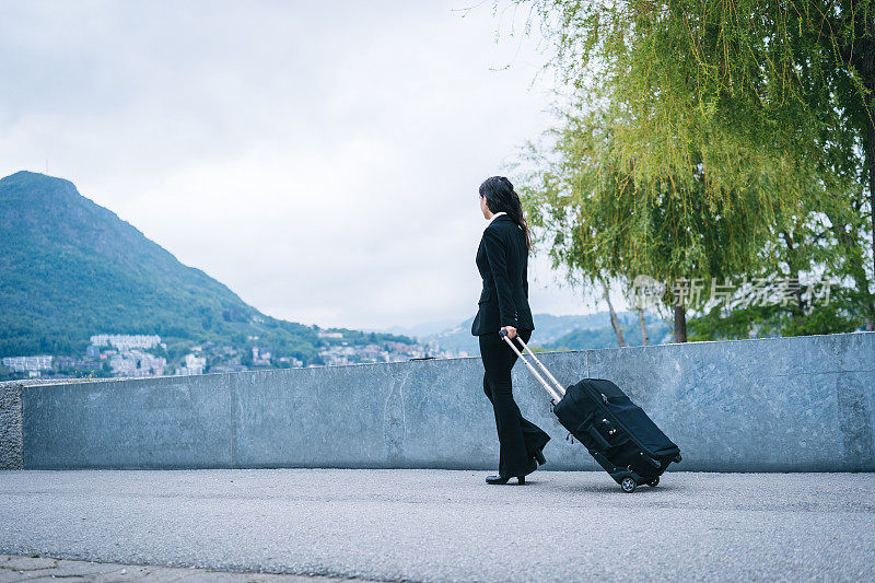 年轻的商务女性带着旅行箱走在户外