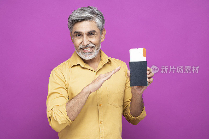 肖像英俊的成熟男子显示护照与票站在孤立的粉红色背景:库存照片