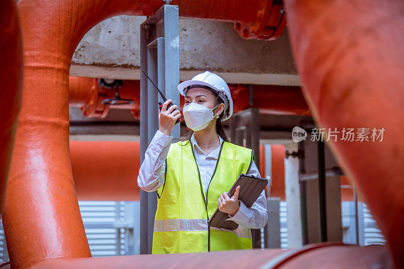 工业工程师在检查大型工业建筑的工业冷却塔空调水冷塔冷风机组HVAC控制空气系统，佩戴口罩保护污染。
