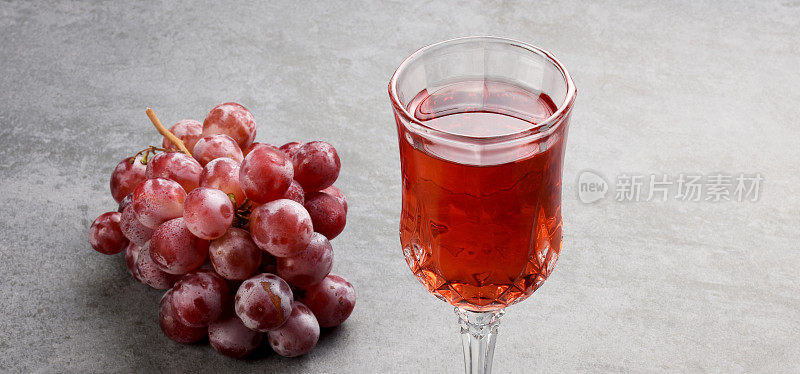 一杯玫瑰红葡萄酒和红葡萄在花岗岩岩石上的质感