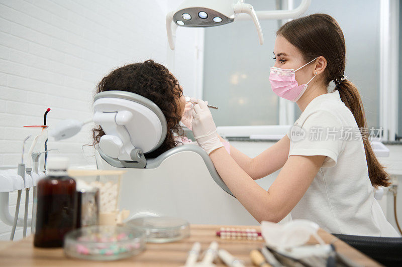 年轻女牙医卫生员，戴防护医用口罩和手套，在现代牙科诊所进行口腔治疗。牙科、口腔护理和口腔卫生概念