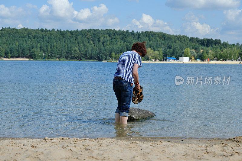 一个女人正在森林湖里洗她的脏脚和凉鞋