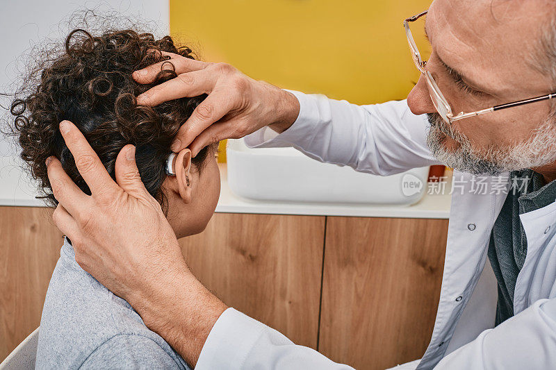 听力学家在访问听力诊所时为男性儿童的耳朵安装助听器。儿童听力解决方案