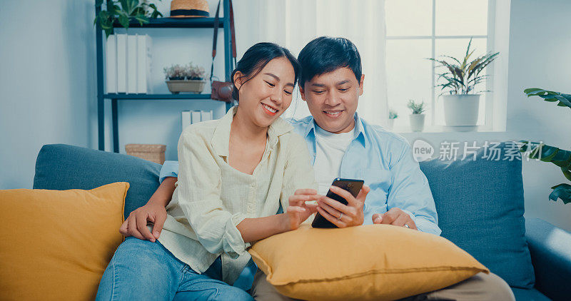 年轻的夫妇休闲地坐在沙发上，在家里的客厅里用智能手机网购。