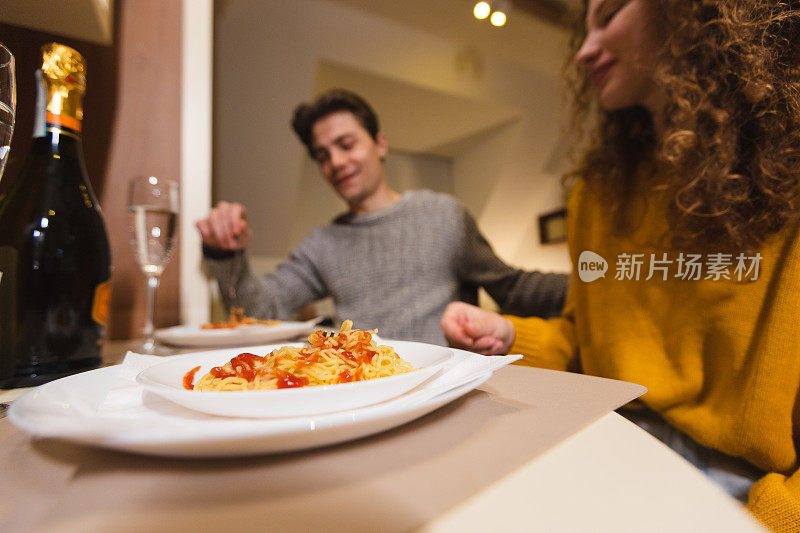 美丽的年轻夫妇在家里喝香槟吃意大利面，享受浪漫的晚餐