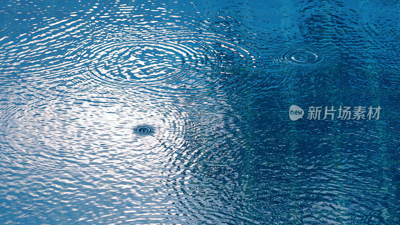雨水落在水池上，阳光反射在表面纹理上。
