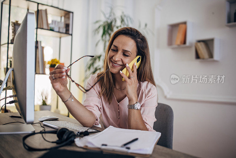 妇女在电脑前工作，在家庭办公室打电话