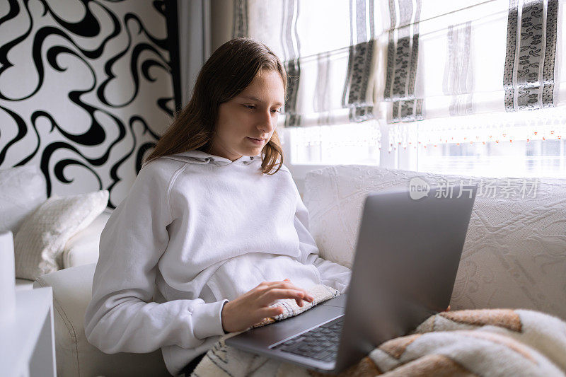 年轻女子舒服地在家里的床上使用笔记本电脑