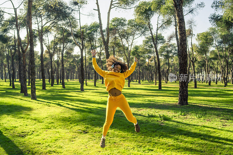一个穿着黄色运动服的女孩在公园里高兴地跳着。