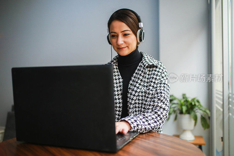 戴着耳机的年轻女子在远离工作场所的地方用笔记本电脑工作