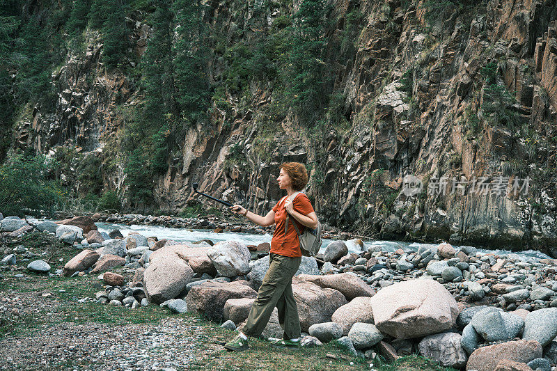 开朗的成熟女游客正在拍摄她在山河岸边徒步旅行的视频