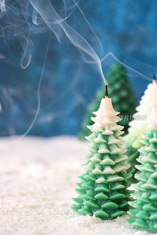 圣诞冷杉森林场景特写图像，人造雪上一组熄灭的圣诞树蜡烛，白色和绿色的吸烟蜡烛，发光的灯芯尖端，斑驳的蓝色背景，重点放在前景上