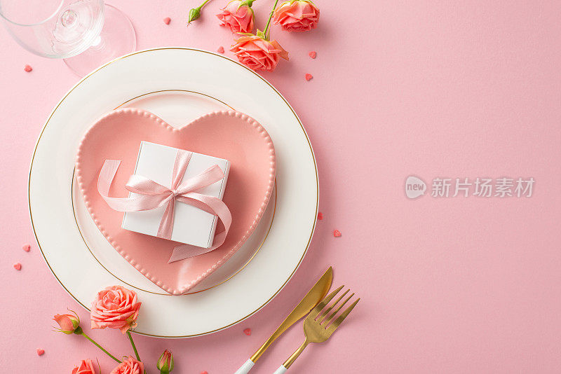 鲜花盛开的爱情:优雅的餐桌布置，心形的盘子，餐具，杯子，玫瑰，撒糖和礼盒，淡粉色的背景。抓住了浪漫的精髓。为文本或广告留出空白空间