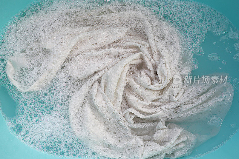 女士的蕾丝裙浸泡在水中，溶解洗涤剂有白色的泡沫。衣服的概念