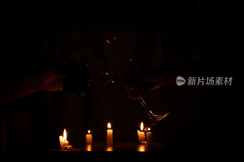 一个女人的手和一个男人的手在家里的烛光下碰杯两杯酒，浪漫的在家庆祝，喝酒