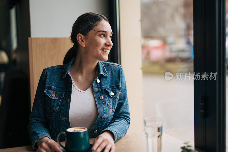 一名年轻女子在咖啡厅享受时光，望着窗外。