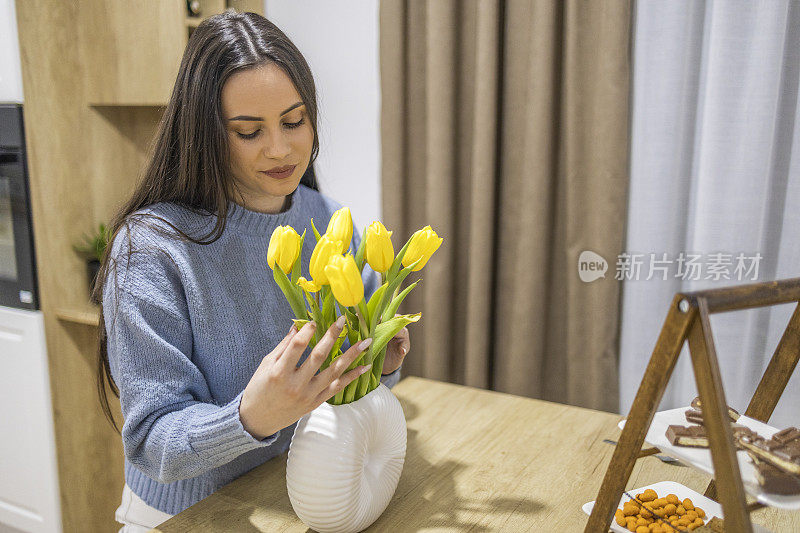 英俊的女孩准备了一束郁金香，她站在厨房柜台前享受着美丽的香味