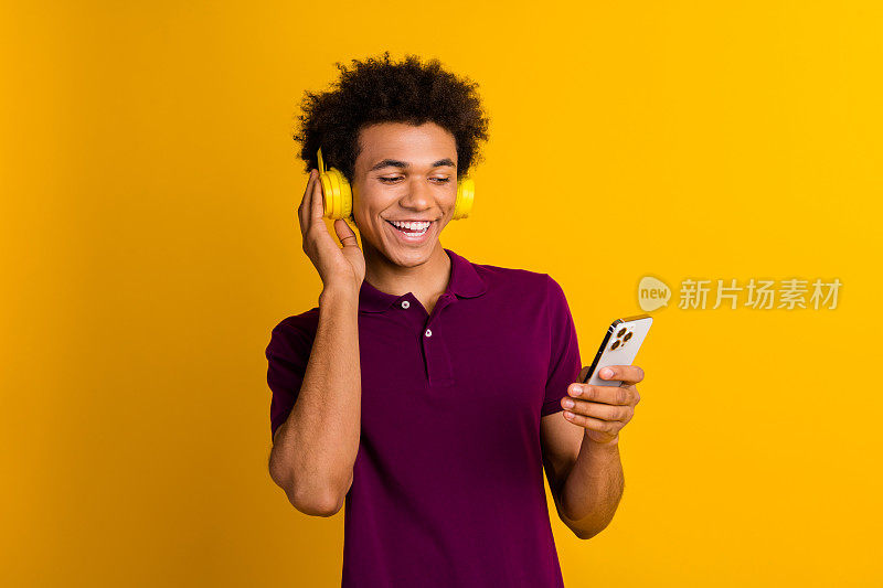 时髦积极的男人穿着时髦的衣服，在黄色背景下用iphone听音频播放列表，阅读社交媒体