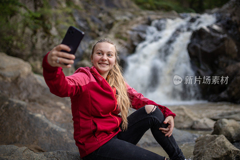 年轻的徒步旅行者在大自然中用手机自拍，背景是美丽的瀑布