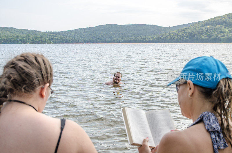 夏日炎炎，一个男人在湖边看着他的女朋友和岳母在湖边的码头上看书