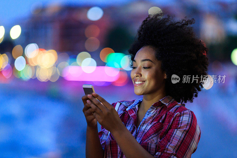 晚上在街上用智能手机微笑的女人