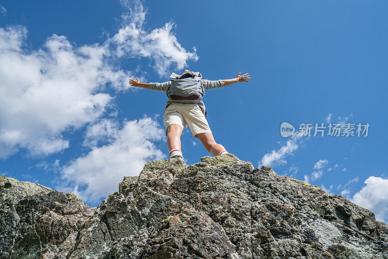 徒步旅行者站在岩石上，双臂伸向天空
