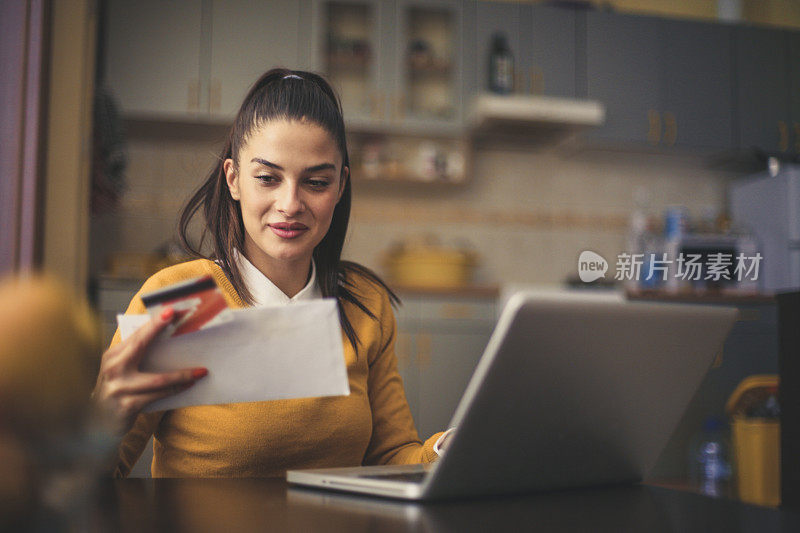 年轻女子拿着信用卡用笔记本电脑阅读文件。