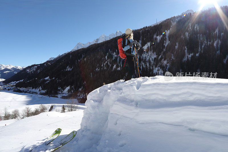 女人扔下滑雪板，在厚厚的积雪中爬上山顶。