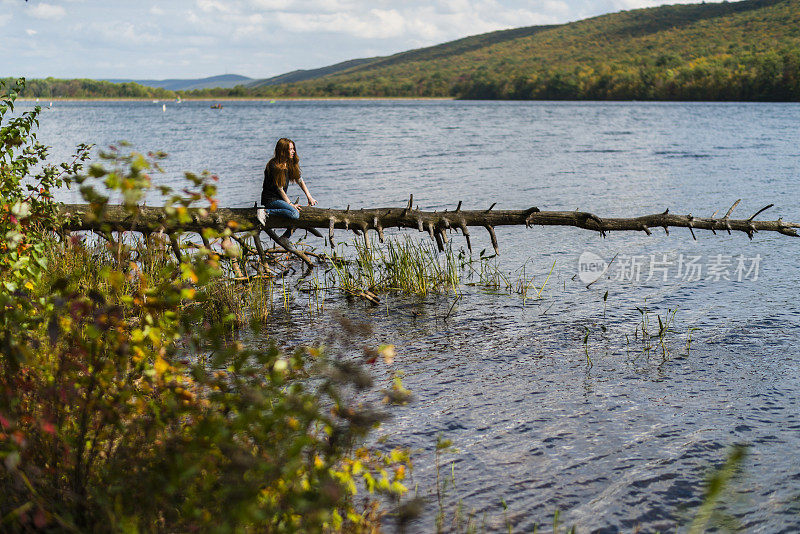 一个少女坐在波科诺斯湖上倒下的树上